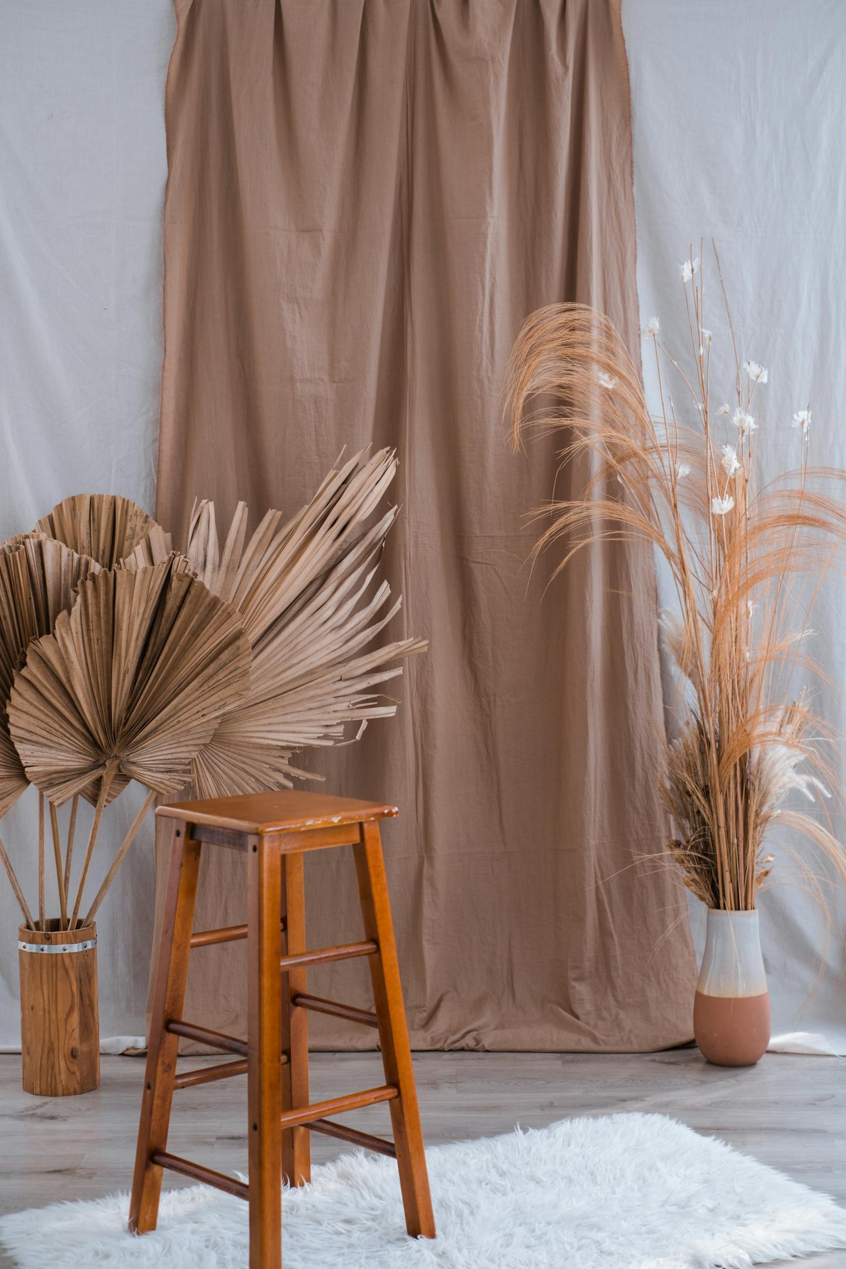 A cozy indoor setting featuring a wooden stool, dried flowers, and a brown curtain backdrop.
