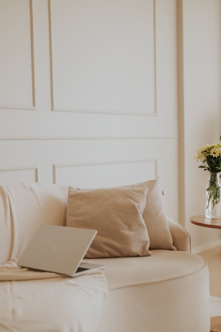 A serene and stylish home office with a neutral aesthetic featuring a laptop and cozy seating.